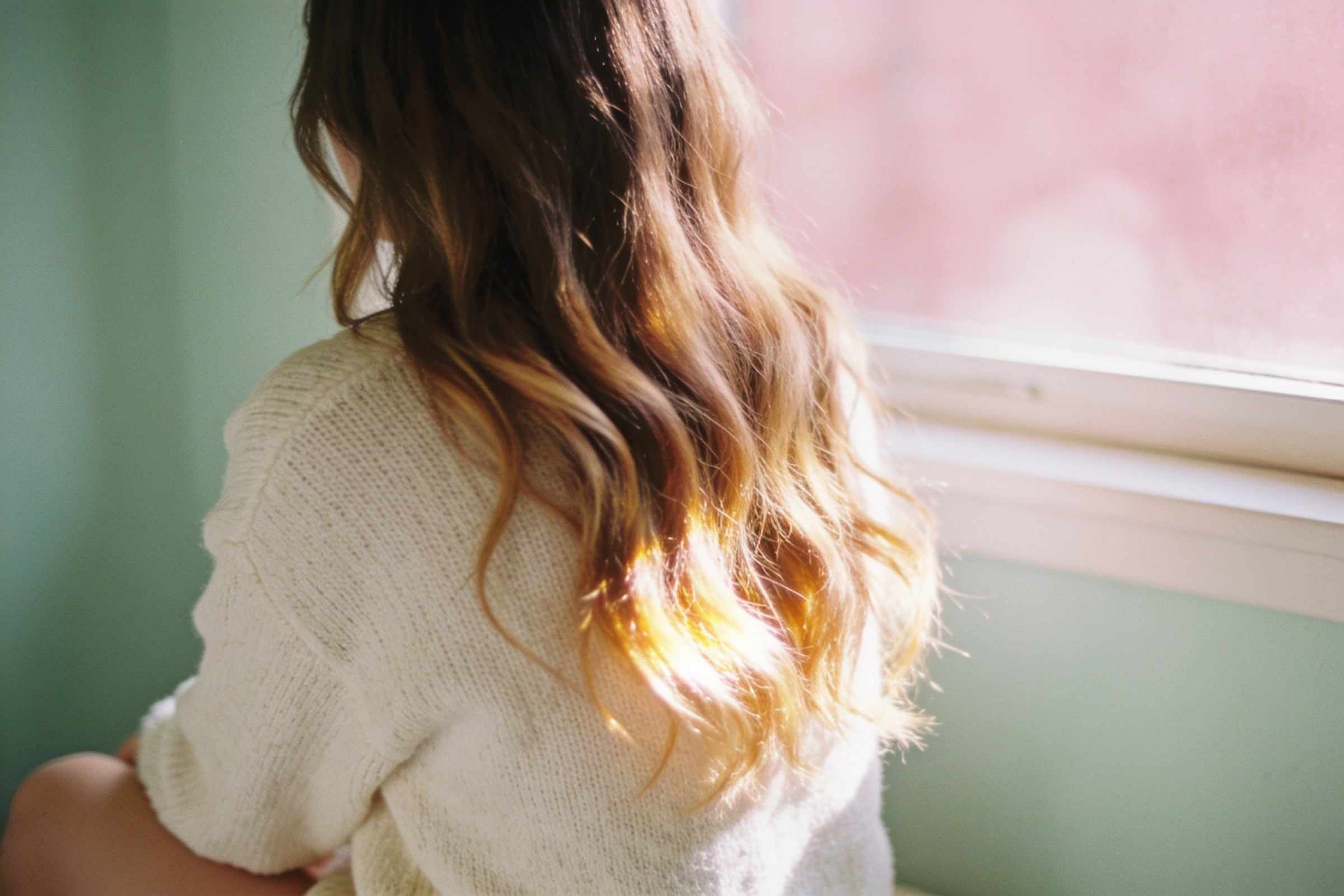 Long hair with soft honey balayage falling in loose waves by a window.