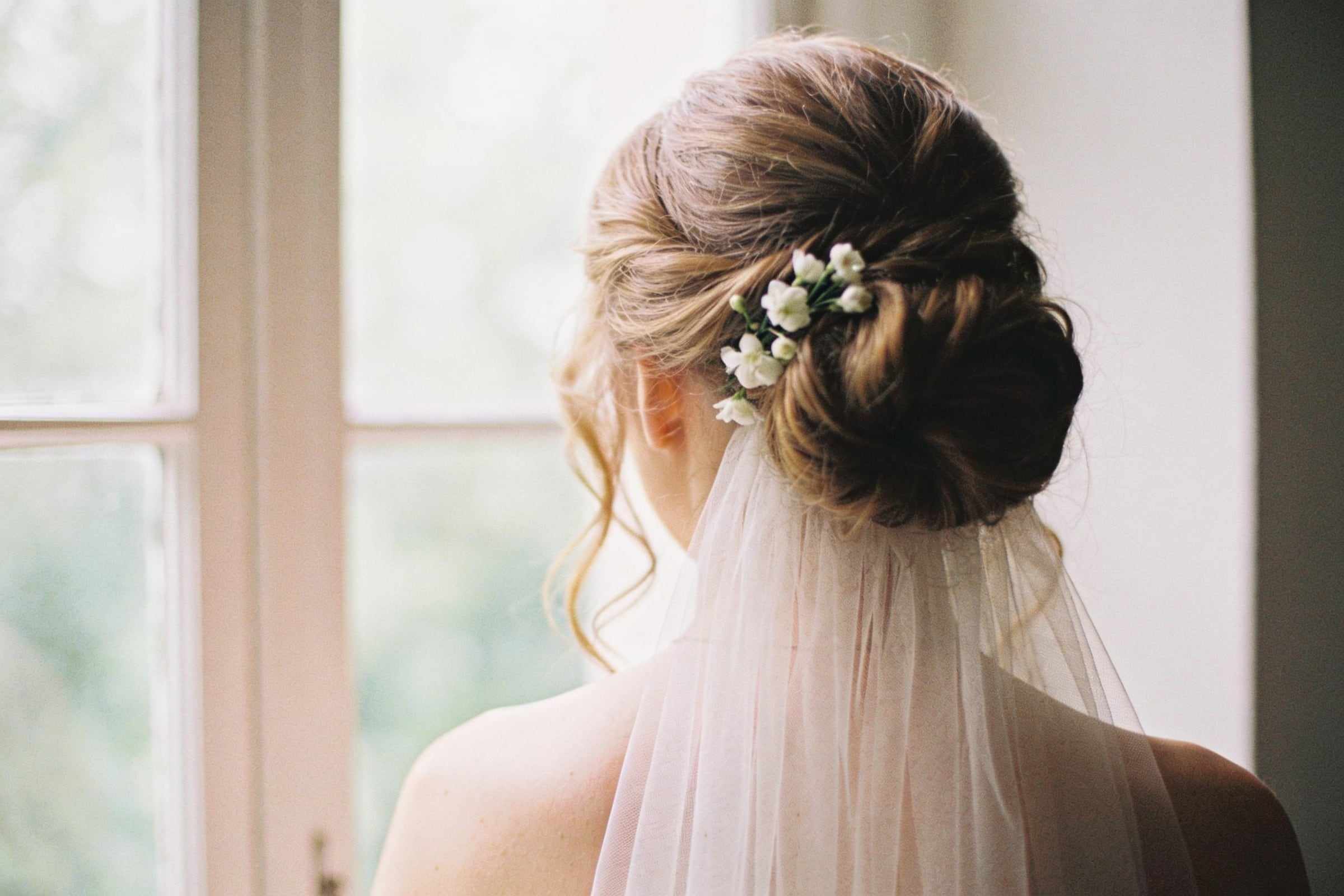 A soft, low bridal bun with loose tendrils, tiny white flowers and a veil.