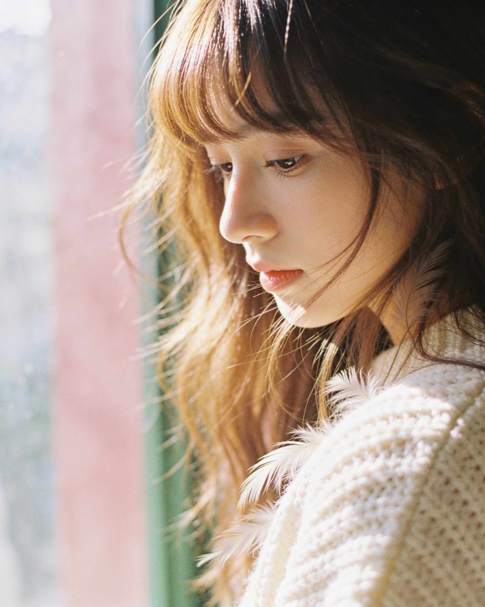 A woman with long feathered layers and soft curtain bangs looking down.