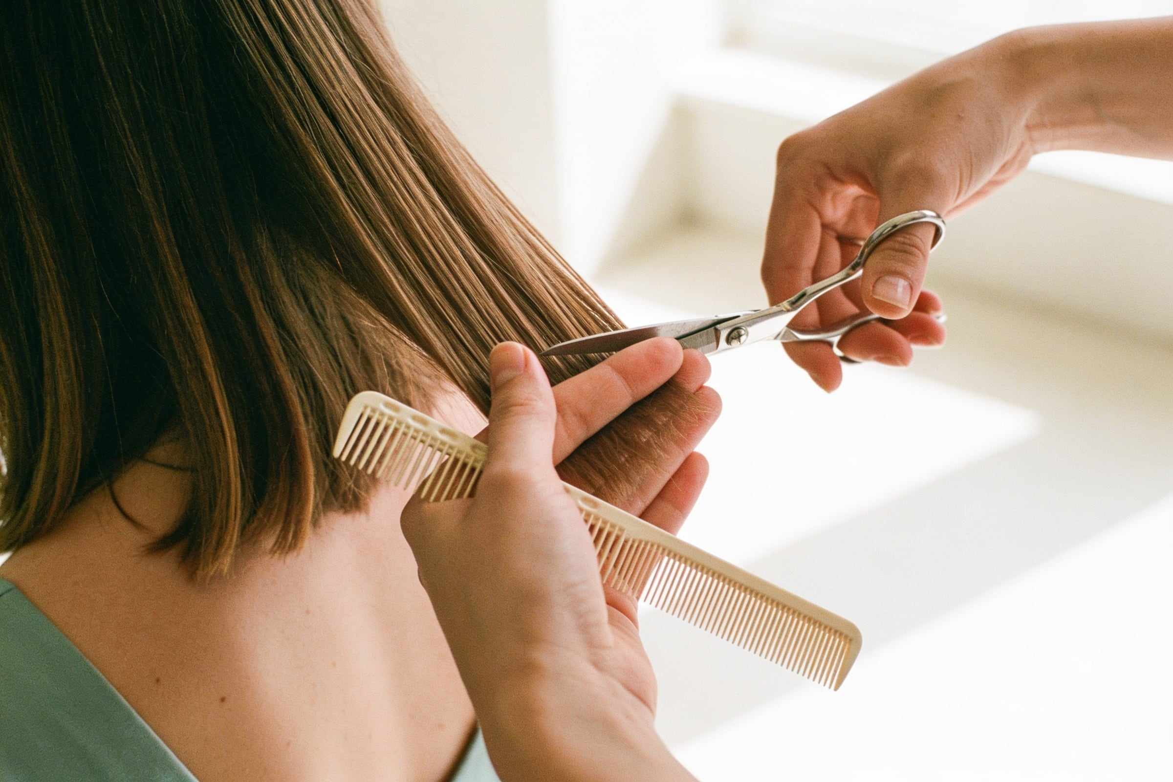 Silver scissors trimming the ends of soft brown hair, a comb between the stylist’s fingers.