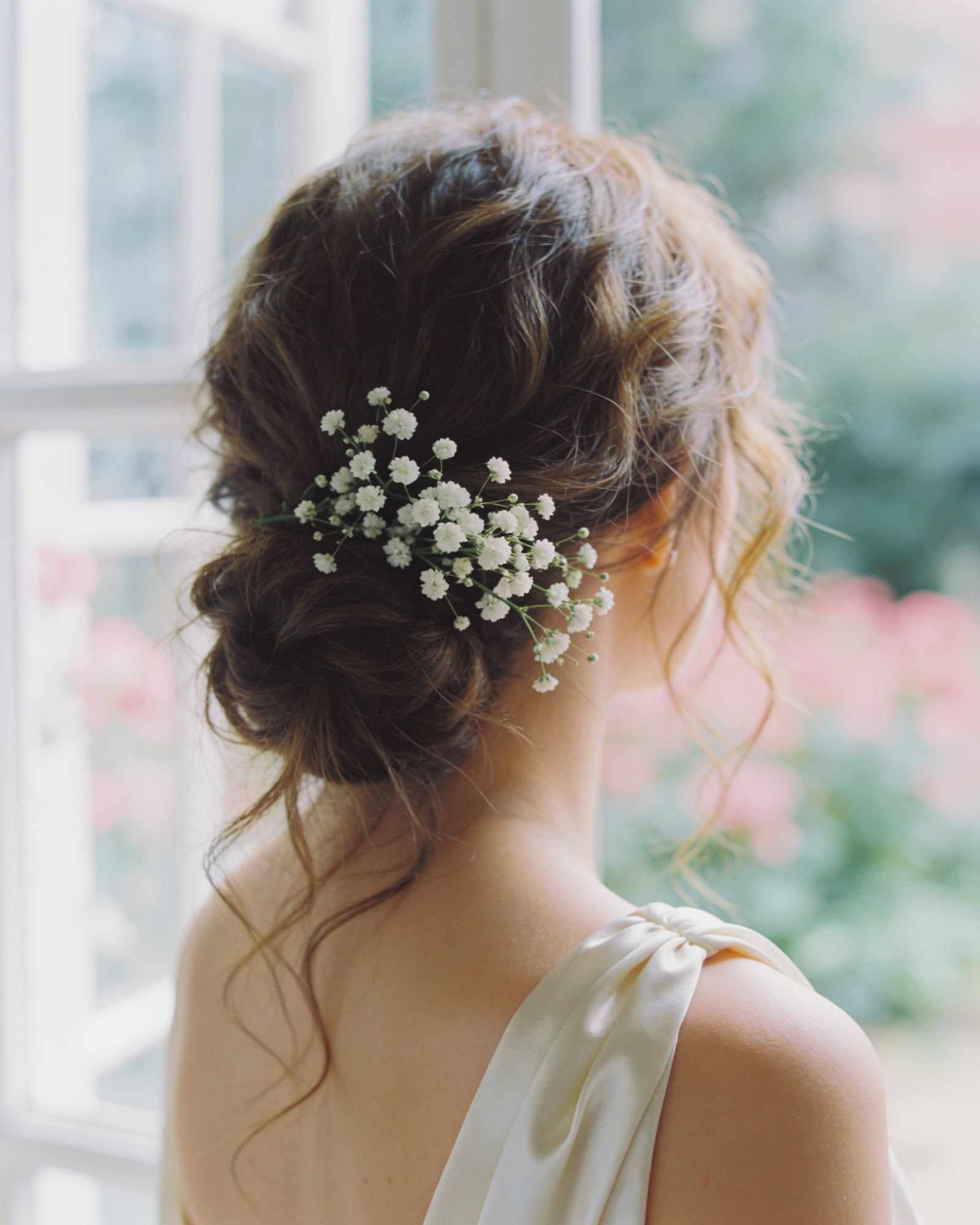 A textured low updo with loose tendrils and white gypsophila.