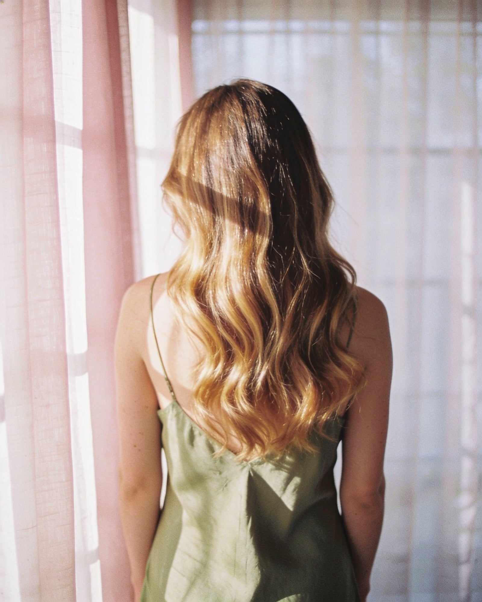 Long hair with a soft honey balayage in loose glossy waves, seen from behind.