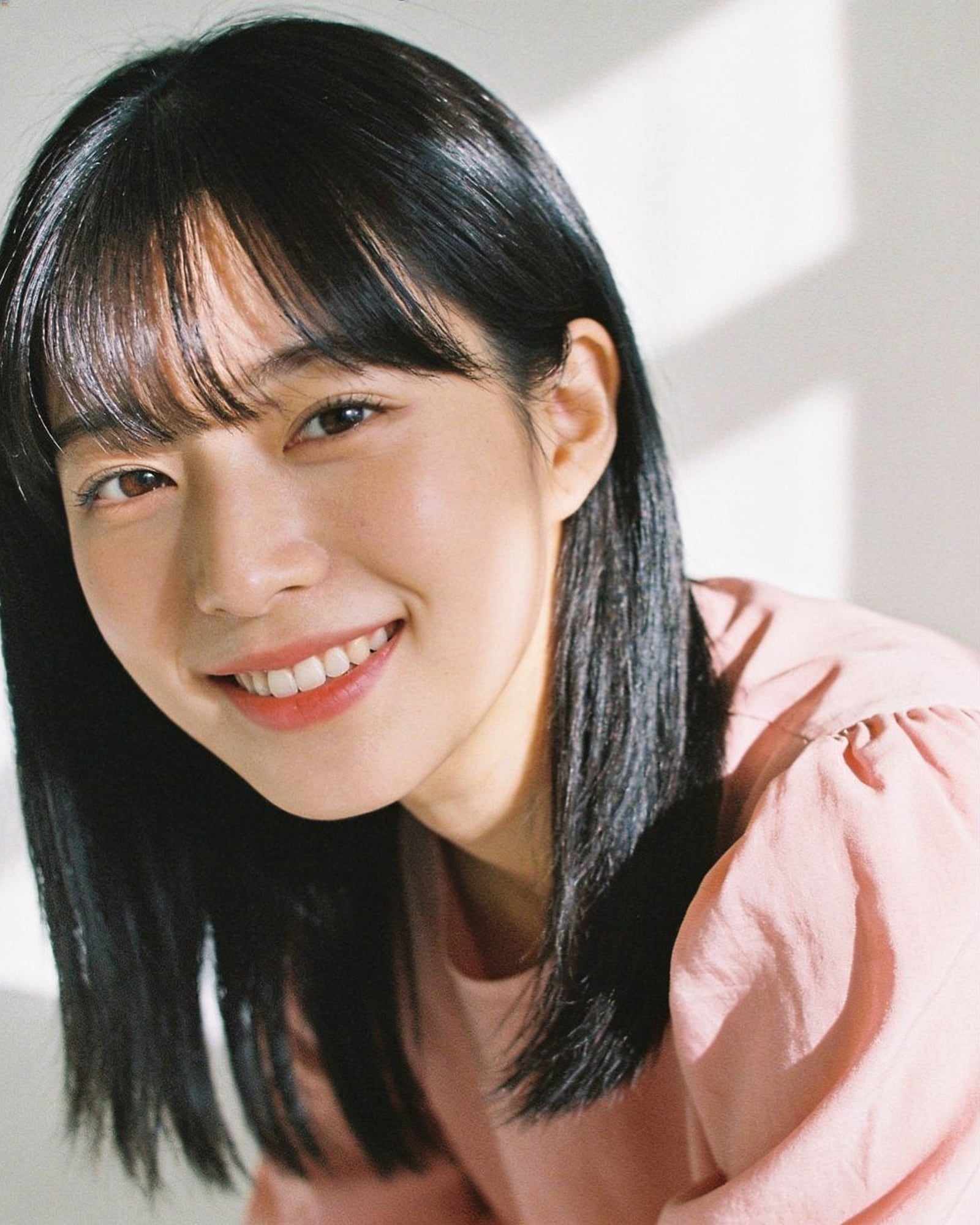 June, with a sleek black bob and curtain bangs, smiling in a blush blouse.
