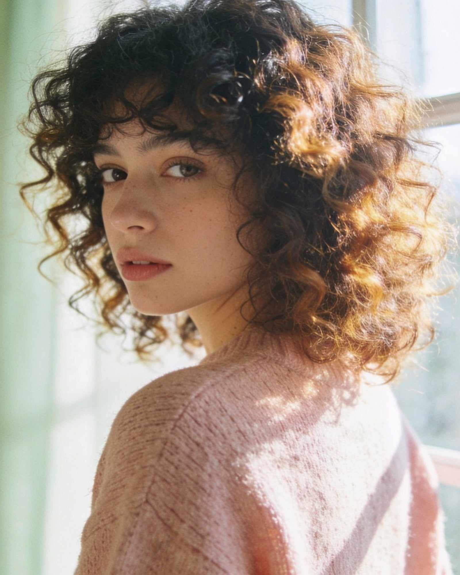 A woman with defined, bouncy dark curls with caramel tips.