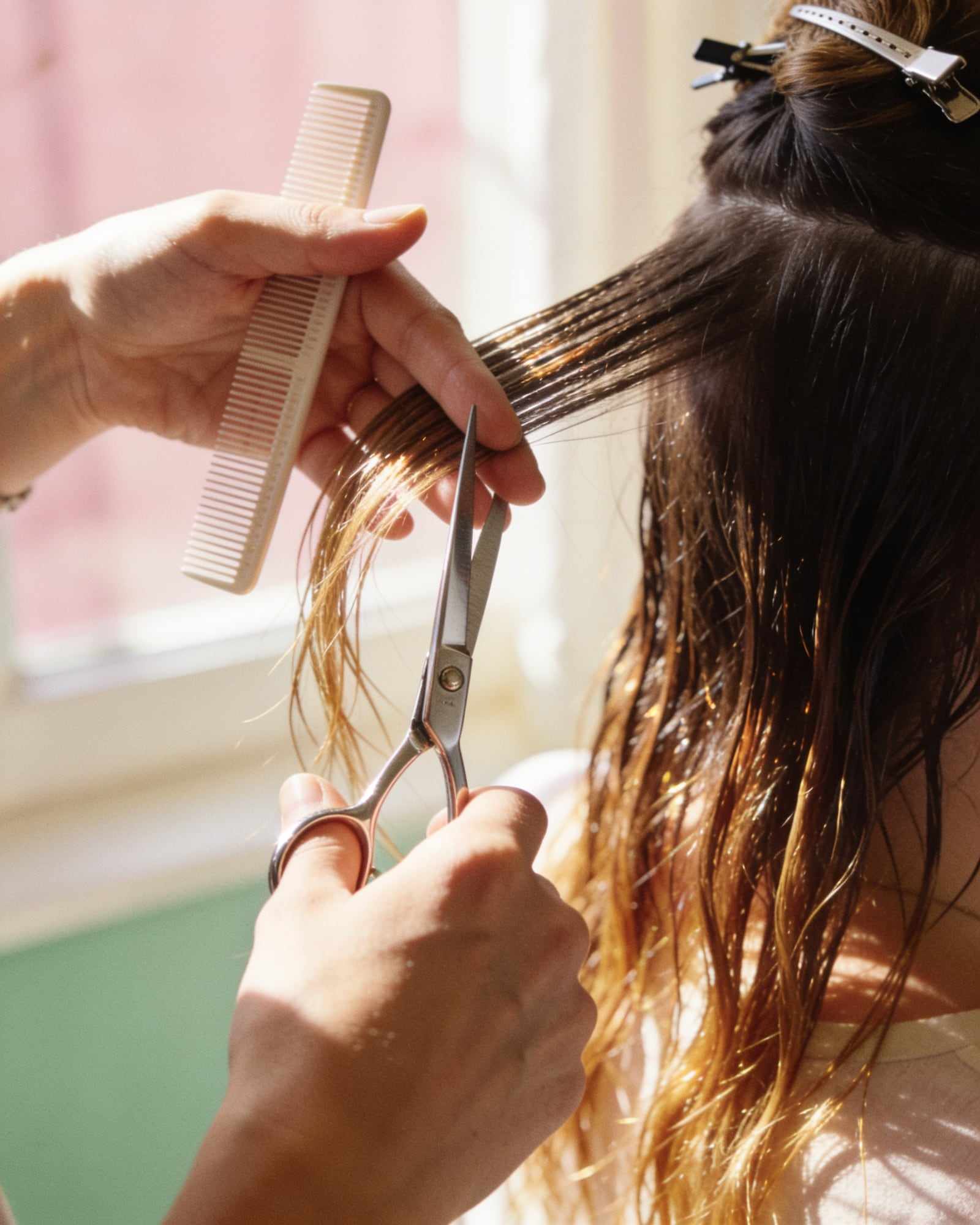 A stylist sections damp hair with a fine comb and scissors.